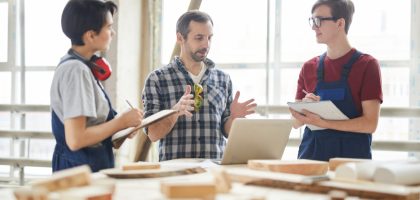 Group of contemporary carpenters discussing project in woodworking shop, copy space
